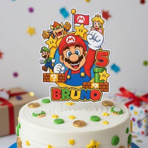 Puede incluir: Un pastel blanco glaseado decorado con monedas de oro, caramelos de champiñones verdes y chispas de estrellas amarillas. Un adorno de pastel colorido presenta a Mario, Luigi, la Princesa Peach y Bowser, con el nombre "BRUNO" y el número "5".