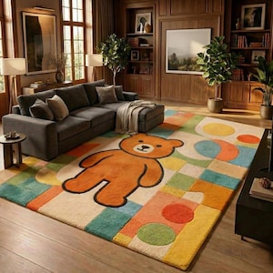 Puede incluir: Una colorida alfombra con un gran diseño de oso de peluche naranja. La alfombra tiene un patrón geométrico con cuadrados y círculos en tonos de amarillo, verde, azul y naranja. La alfombra está en un salón con un sofá seccional gris.