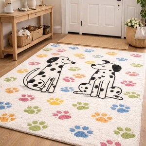 May include: A cream-colored area rug featuring two Dalmatian dog illustrations with black spots. The rug is decorated with colorful paw prints in pink, yellow, green, and blue. The rug is placed in a home entryway.