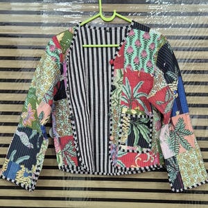 May include: A long-sleeve quilted jacket featuring a patchwork design with various floral, palm leaf, and geometric patterns in shades of green, red, pink, and blue. The jacket has a black and white vertical striped interior and front trim.