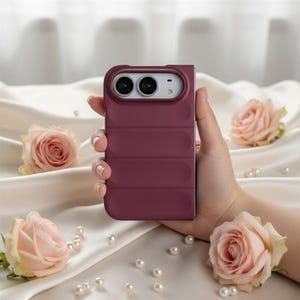 Peut inclure: Une coque de smartphone bordeaux profond avec une texture matelassée horizontale de style doudoune. La coque présente une découpe rectangulaire pour l'appareil photo en haut avec deux objectifs circulaires, conçue pour un appareil mobile pliable.