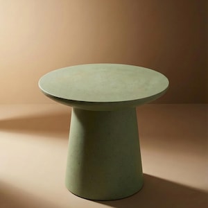 May include: A sage green side table with a round top and a conical base. The table is made of a speckled material and is suitable for indoor or outdoor use. The table's height is approximately 18 inches.