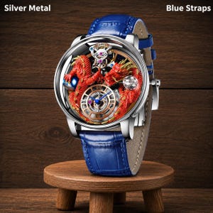 Op de afbeelding: Een zilveren metalen polshorloge met een blauwe leren band. De wijzerplaat van het horloge heeft een rood drakenontwerp en een goudkleurige wijzerplaat met blauwe wijzers. Het horloge wordt tentoongesteld op een kleine houten standaard.