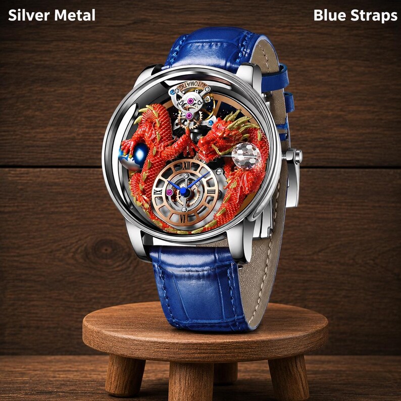 Op de afbeelding: Een zilveren metalen polshorloge met een blauwe leren band. De wijzerplaat van het horloge heeft een rood drakenontwerp en een goudkleurige wijzerplaat met blauwe wijzers. Het horloge wordt tentoongesteld op een kleine houten standaard.