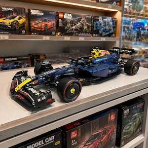 May include: A detailed building block model of a dark blue and black Formula 1 race car featuring yellow accents, sponsor logos including Bybit, Mobil, and Claro, and black tires with red trim. The model is displayed on a shelf in a retail store.