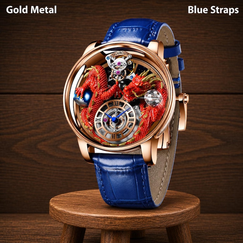 Op de afbeelding: Een goudkleurig polshorloge met een blauwe leren band. De wijzerplaat van het horloge heeft een rood drakenontwerp en zichtbare tandwielen. Het horloge heeft een ronde wijzerplaat en Romeinse cijfers.