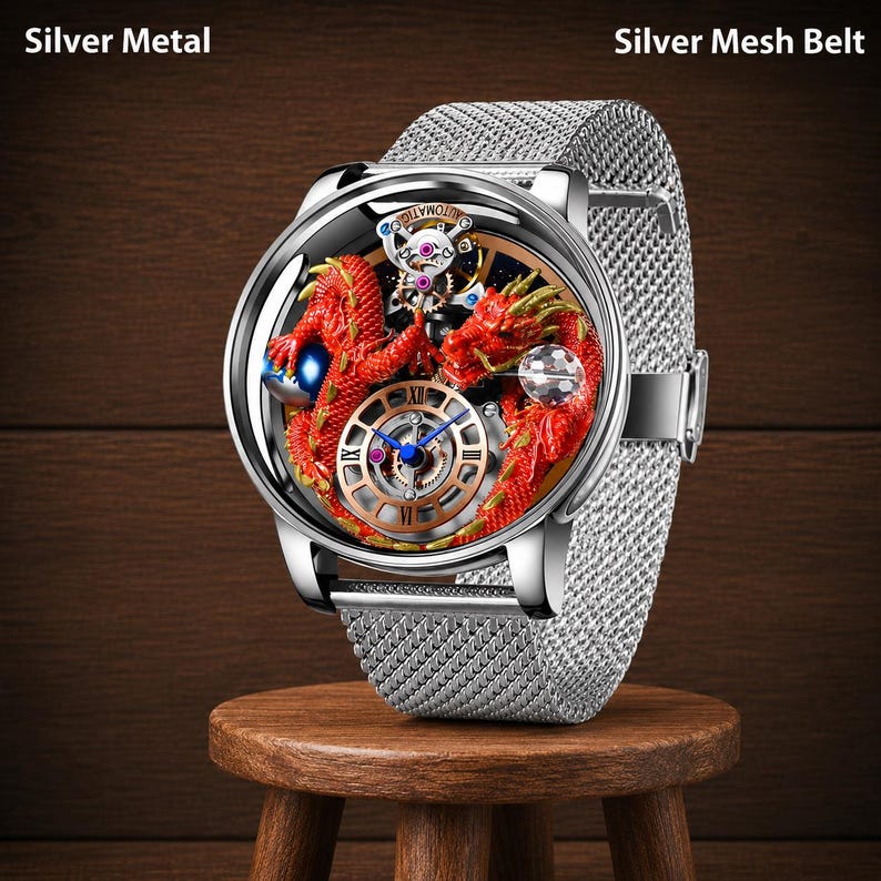 Op de afbeelding: Zilveren metalen polshorloge met een zilveren mesh band. De wijzerplaat van het horloge heeft een rood drakenontwerp met gouden accenten en zichtbare interne tandwielen. Het horloge wordt getoond op een kleine houten kruk.