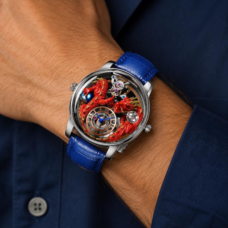 Op de afbeelding: Een luxe polshorloge met een zilveren kast en een blauwe leren band. De wijzerplaat toont een gedetailleerd rood drakenontwerp met zichtbare mechanische componenten. Het horloge heeft een blauwe wijzerplaat en een kleine, decoratieve edelsteen.