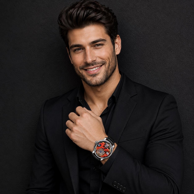 Op de afbeelding: Een zwart pak met een zwart overhemd. Een zilveren horloge met een zwarte leren band en een rode en zilveren wijzerplaat is zichtbaar. De wijzerplaat van het horloge heeft gedetailleerde mechanische elementen.