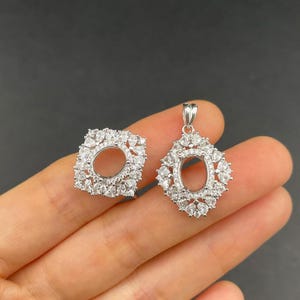 Peut inclure: Deux montures de bijoux argentées, une carrée et une ovale, toutes deux incrustées de petites pierres précieuses transparentes. Les montures ont des centres ouverts, conçus pour contenir une pierre précieuse ou un autre élément décoratif. La monture ovale a une boucle pour une chaîne.