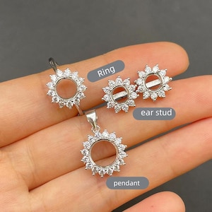 Può includere: Un set di gioielli composto da un anello, un pendente e orecchini. Ogni pezzo presenta un design circolare con un alone di piccole pietre trasparenti. L'anello ha una singola fascia, il pendente ha un'asola e gli orecchini hanno perni.