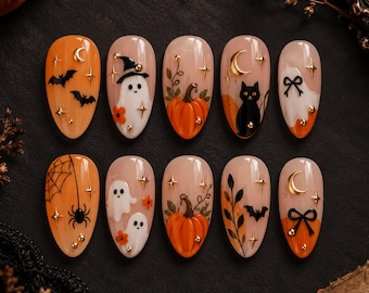 Może przedstawiać: Zestaw dziesięciu migdałowych sztucznych paznokci z motywami halloweenowymi, takimi jak pomarańczowe dynie, białe duszki, czarne koty, nietoperze, pajęczyny, złote półksiężyce, gwiazdki i czarne kokardki, ozdobione małymi złotymi metalowymi ćwiekami.