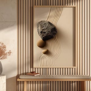 Peut inclure: Une œuvre d'art encadrée représentant un jardin zen avec une grande roche grise texturée et deux petites pierres sphériques. L'œuvre est suspendue au-dessus d'un banc en bois avec un coussin gris. Un vase avec des plantes séchées est posé sur une table d'appoint cylindrique.