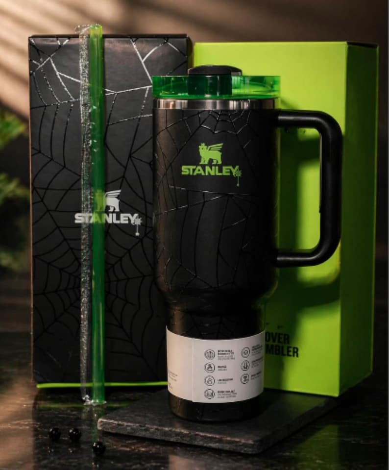 Peut inclure: Gobelet Stanley noir avec un couvercle et une poign&eacute;e verts, orn&eacute; d'un motif de toile d'araign&eacute;e. Le logo Stanley est en vert. Le gobelet est emball&eacute; avec une bo&icirc;te noire avec un motif de toile d'araign&eacute;e et une paille verte.