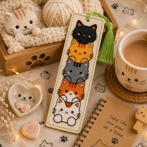 Adorable cat stack cross stitch bookmark pattern featuring five kawaii cats peeking one above another in black, orange, gray, orange-and-white, and white colors. This cute animal bookmark design is stitched with 9 DMC colors and measures 40 × 125 stitches. Perfect for cat lovers, bookworms, and beginner to intermediate cross stitch enthusiasts. Ideal as a handmade reading accessory, thoughtful gift, or DIY embroidery project with instant PDF download for creating a charming bookmark.