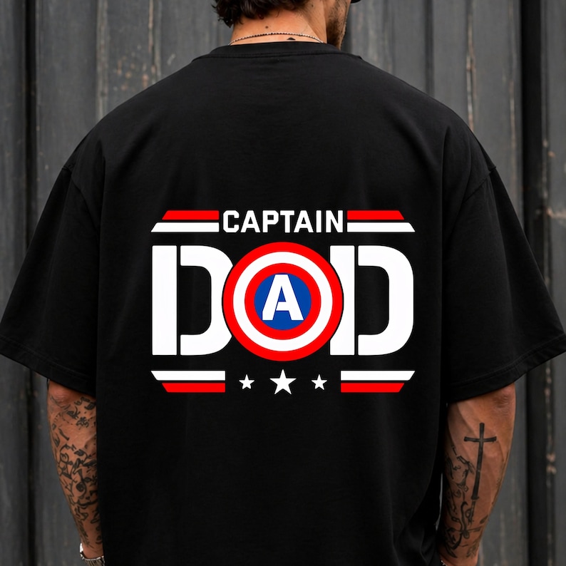 May include: A black short-sleeved t-shirt featuring a graphic on the back with the text CAPTAIN DAD in white letters. The letter O is replaced by a circular shield design in red, white, and blue with a white letter A in the centre.