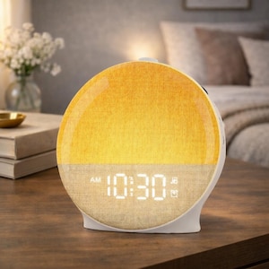 Könnte beinhalten: Ein weiß-beiger digitaler Wecker mit einer gelb-beigen stoffbezogenen Oberfläche. Die Uhr zeigt "10:30 AM" in weißen Digitalziffern an. Die Uhr steht auf einer Holzoberfläche.