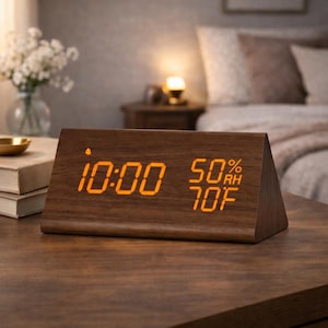 May include: A wooden digital alarm clock displaying the time as 10:00, 50% humidity, and 70°F. The clock has a triangular shape and a warm, orange digital display. The clock is on a dark wooden surface.