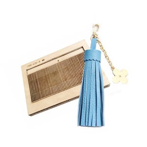 May include: A light blue leather tassel keychain with a gold-colored chain and a four-leaf clover charm. A wooden die-cut tool with the text "200-120-4" is also in the image. The die-cut tool has a rectangular shape with parallel grooves.