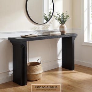 May include: A black console table with a decorative design, a round mirror, and a woven basket. The table has a dark finish and is topped with books and a decorative tray. A vase with greenery sits on the table.