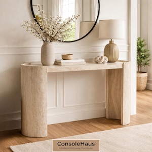 May include: A beige console table with a curved design, holding a vase of white flowers, a lamp, and decorative items. A round mirror hangs above the table. The text "ConsoleHaus Modern Entryway Furniture" is at the bottom.