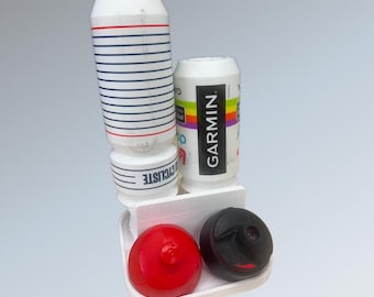 May include: A white plastic storage rack holding two water bottles and two bottle caps. One bottle is white with blue and red horizontal stripes and the text CYCLISTE, while the other is white with a Garmin logo and colorful accents. Two caps are red and black.