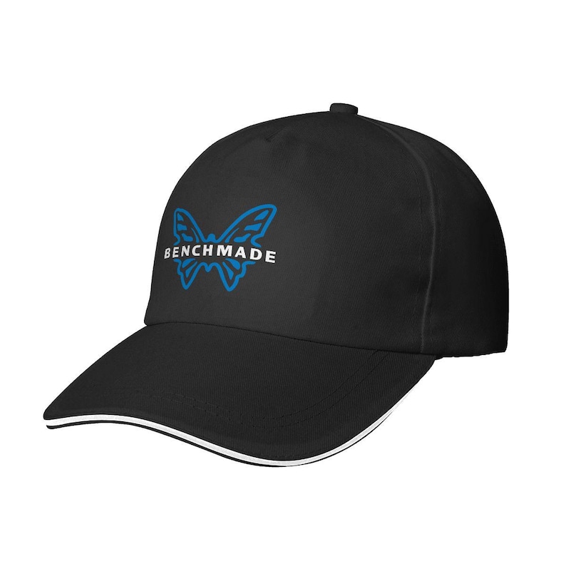 Puede incluir: Gorra de b&eacute;isbol negra con visera curva y ribete blanco. La gorra presenta un logotipo de mariposa azul con la palabra "BENCHMADE" en blanco. Fabricada con material duradero, ideal para actividades al aire libre.