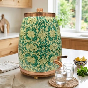 May include: A cylindrical beverage dispenser featuring a vibrant green body with a repeating cream-colored floral pattern. It includes a copper-toned lid and base, a matching copper spigot, and rests on small feet. The design is upright and sturdy.