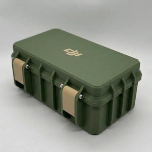 May include: An olive green rectangular case with a ridged design and a flat top. The case has two tan-coloured latches and a silver logo on the top. The case is designed to protect the contents inside.