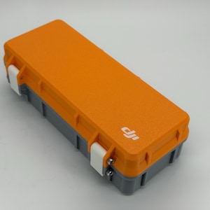 May include: A rectangular orange and grey case with white clasps. The case has a textured surface and a small white logo on the top. The case is designed to protect the contents inside.