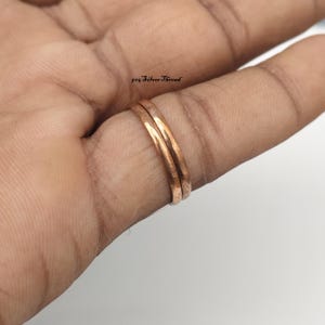Könnte beinhalten: Zwei dünne, glatte, polierte kupferfarbene Metallringe, die zusammen an einem Finger getragen werden. Die Metallbänder haben einen warmen Glanz und ein einfaches, abgerundetes Profil. Der Text 925 SilverThread ist im Hintergrund zu sehen.