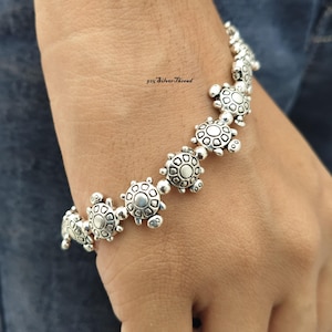 Könnte beinhalten: Ein silberfarbenes Armband mit einer Reihe von aneinandergereihten schildkrötenförmigen Anhängern. Jeder Schildkrötenanhänger hat ein detailliertes Panzer-Muster und einen kleinen Kopf. Der Text 925 SilverThread ist in der Mitte zu sehen.