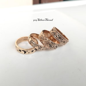 Könnte beinhalten: Vier roségoldfarbene Metallringe in einer Reihe angeordnet, mit eingravierten Mustern wie Sternen, einem Halbmond, Blumenmotiven und komplexen Schnörkeln. Der Text 925 SilverThread ist über den Ringen auf der weißen Fläche sichtbar.