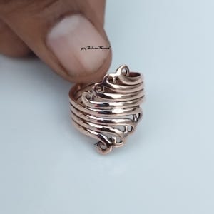 Op de afbeelding: Een roségoudkleurige ring met een meerlaags, wervelend ontwerp dat om de vinger wikkelt. Het metalen oppervlak is gepolijst en reflecterend, waardoor een reeks onderling verbonden, gebogen banden ontstaat. De tekst 925 SilverThread is zichtbaar.