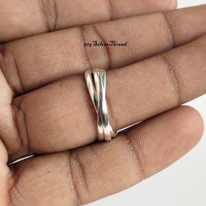 Op de afbeelding: Een zilveren ring met een ontwerp van drie banden met in elkaar verstrengelde, gepolijste metalen strengen. De ring is gemarkeerd met de tekst 925 SilverThread, wat de samenstelling aangeeft. De band heeft een gladde, reflecterende afwerking.