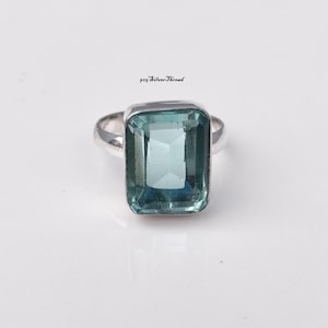 May include: A silver ring featuring a large, rectangular, faceted light blue gemstone set in a polished metal band. The text 925 SilverThread is printed in small black letters above the ring, indicating the metal composition and brand name.