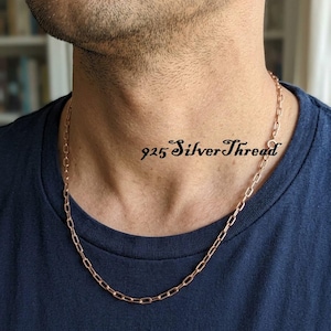 May include: A rose gold-toned chain necklace featuring elongated rectangular links. The chain rests around the neck, and the text 925 SilverThread is visible in black script font near the center of the necklace chain against the skin.