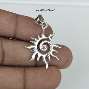 May include: A shiny silver pendant shaped like a stylized sun with a central spiral and radiating flame-like points. The pendant features a triangular bail at the top for attachment. The text 925 SilverThread is visible above the pendant.