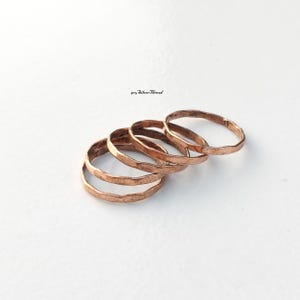 May include: A set of five copper-coloured rings with a hammered, textured finish. The rings are arranged in a slightly overlapping, cascading formation. The text 925 Silver Thread is visible in small black font above the rings.