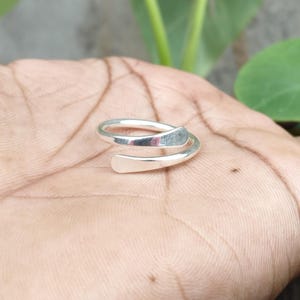 以下が含まれることがあります： 滑らかでオープンなデザインのポリッシュ仕上げシルバーカラーのバイパスリング。わずかに平らで丸みを帯びた2つの端が重なり合っており、連続的で洗練された光沢のある金属製のバンド構造を作り出しています。