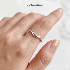 Puede incluir: Un anillo de plata 925 pulida con un diseño ondulado suave y continuo que se curva sobre el dedo. La banda tiene un acabado metálico reflectante y está marcada con el texto 925 SilverThread en la parte superior de la imagen.