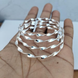 Op de afbeelding: Een set van vier gestapelde zilveren armbanden, elk met een doorlopend gedraaid spiraalontwerp. Het metaal heeft een gepolijste, reflecterende afwerking. De tekst 925 SilverThread is zichtbaar in het midden van de gestapelde armbanden.