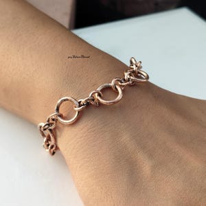 Pode incluir: Uma pulseira de corrente em tom de ouro rosa com uma série de elos circulares interligados com um acabamento texturizado e ligeiramente desgastado. A superfície metálica apresenta um tom de cobre quente. O texto 925 SilverThread é visível.
