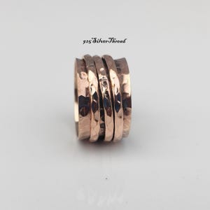May include: A wide copper-toned spinner ring featuring a hammered, textured surface with three distinct bands. The ring is displayed upright with the text 925 SilverThread positioned above it. The metal has a warm, metallic finish with dark indentations.