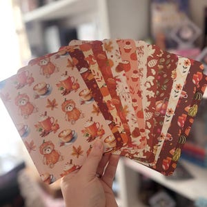 May include: A collection of rectangular cards featuring autumn-themed patterns. The designs include illustrations of teddy bears wearing pumpkin costumes, mugs of coffee with whipped cream, cinnamon sticks, maple leaves, and various seasonal gourds.