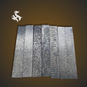 Può includere: Un assortimento di otto pezzi metallici rettangolari con intricati motivi a vortice in tonalità argento e grigio. I pezzi sono disposti verticalmente, mostrando varie trame e design. Un logo di drago bianco si trova nell'angolo in alto a sinistra.