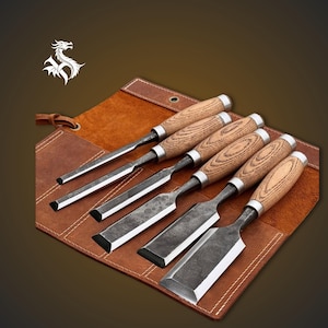 May include: A collection of six wood chisels with wooden handles and metal blades, displayed on a brown leather tool roll. The chisels are of different sizes and blade styles, suitable for carpentry.