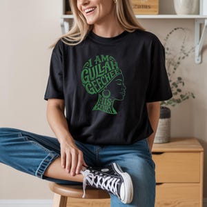 May include: Black t-shirt featuring the green text "I AM GULLAH GEECHEE HIS STORY" and a woman's profile. The shirt is worn with blue jeans and black high-top trainers.