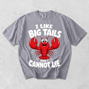 May include: A grey t-shirt with a cartoon red lobster and the white text "I LIKE BIG TAILS and I CANNOT LIE". The lobster has large red claws and a smiling face. The t-shirt is a casual style.