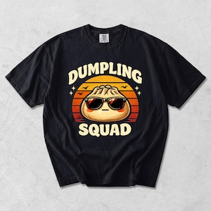 Puede incluir: Camiseta negra con un dibujo de una bola de masa con gafas de sol, sobre un fondo de puesta de sol. El texto "DUMPLING SQUAD" está arqueado arriba y abajo del dibujo. La camiseta tiene cuello redondo y mangas cortas.
